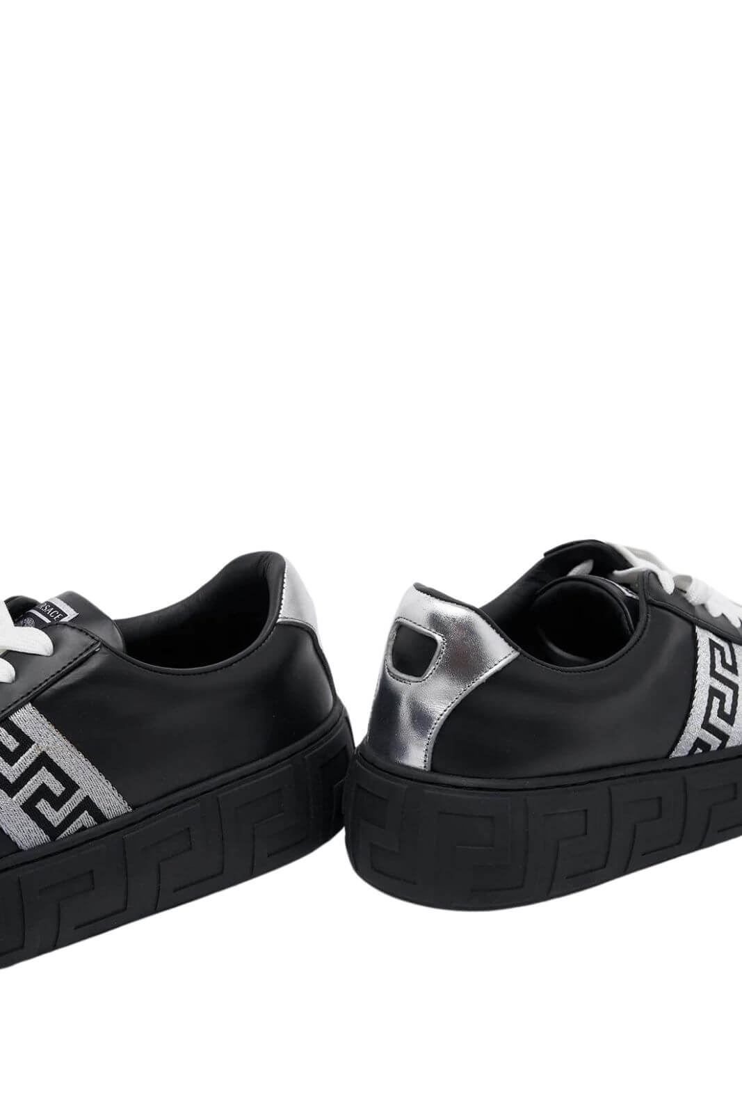 A pair of black Versace Greca sneakers with silver accents and a lace-up closure.
